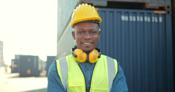 Handsome and happy professional African engineers worker wearing safety vest and hard hat charmingly smiling on camera. In the warehouse background looking confidently.