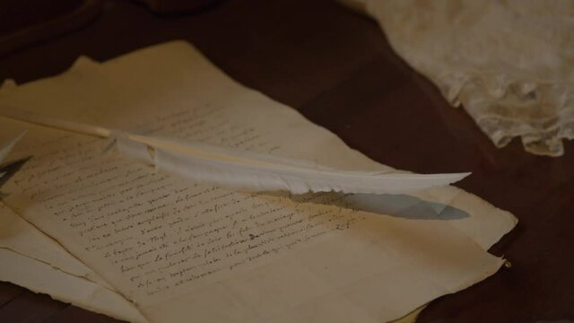 Close pan over quill lying on old letter on a antique desk