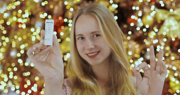 Antigen test negative result. Young woman show self-test smiling to camera. Getting negative COVID-19 PCR test. Woman in front of Christmas tree with lights on bokeh. Test with no logo