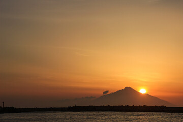 夕陽に染まる海と山影に沈む太陽
