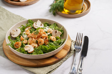 Arugula salad with shrimp and champignons, olive oil and dill on a wooden board on a white surface