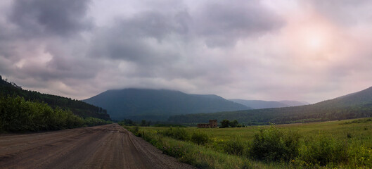 Picturesque dirt road with mountains on the horizon and a green meadow.