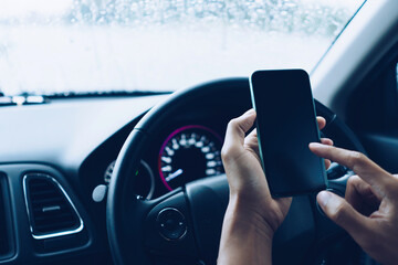Hand of woman on steering wheel drive a car while using smartphone.