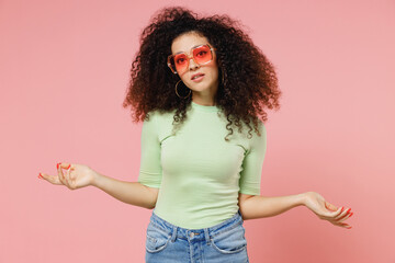 Puzzled young curly latin woman 20s years old wears mint t-shirt sunglasses spread hands shrugging...