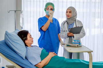 Asian female nurse in face mask blue uniform shake and checking blood sample in test tube while Muslim Islam Arab doctor in white lab coat with hijab and stethoscope writing symptom of senior patient