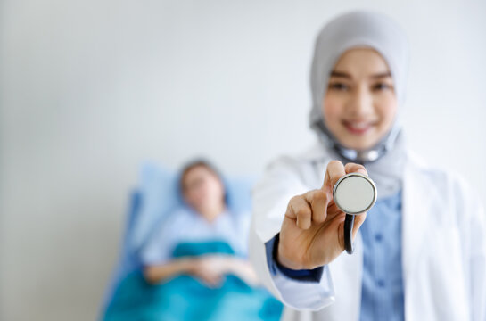 Closeup shot of stethoscope equipment ready to listen heartbeat pulse of patient in Muslim Islam Arab female doctor finger and hand wearing white lab coat hijab standing smiling in blurred background