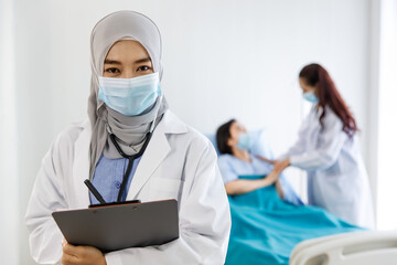 Portrait closeup shot of Muslim Arab Islam female doctor in white lab coat and hijab with stethoscope standing writing analysis data information on clipboard while Asian doctor checkup senior patient
