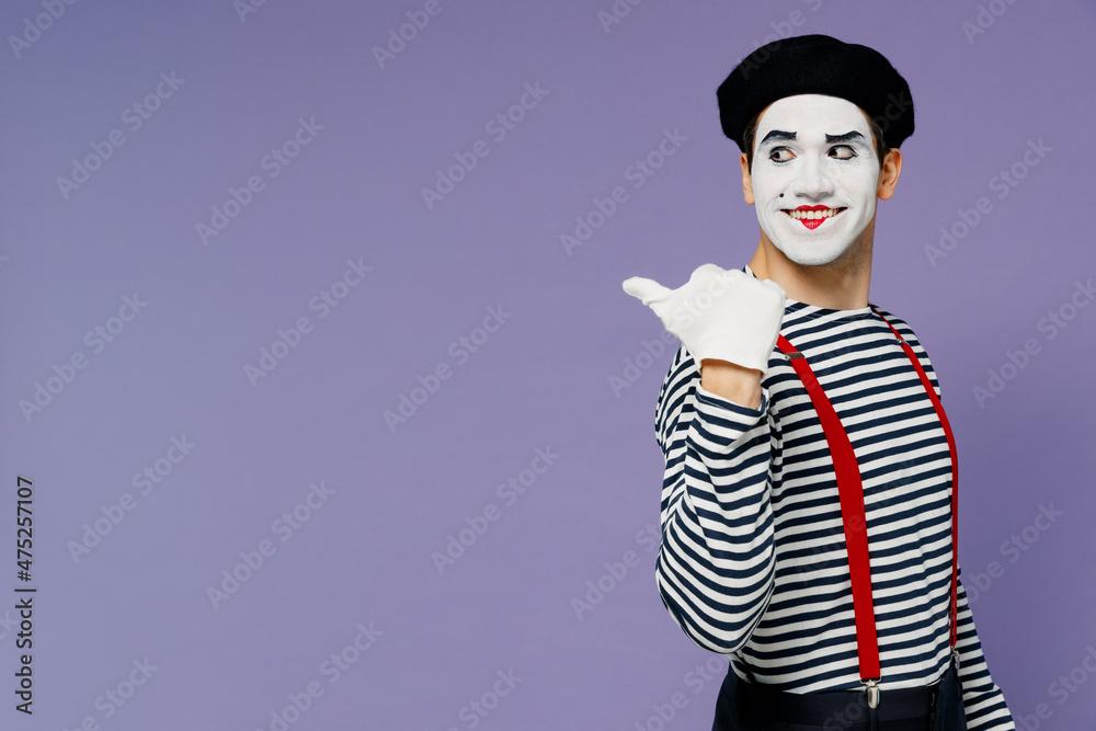 Wall mural Smiling young mime man with white face mask wears striped shirt beret point finger looking back on workspace area copy space mock up isolated on plain pastel light violet background studio portrait.