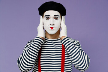 Charismatic amazing ecstatic young mime man with white face mask wears striped shirt beret cover ears with hands do not want to listen isolated on plain pastel light violet background studio portrait.