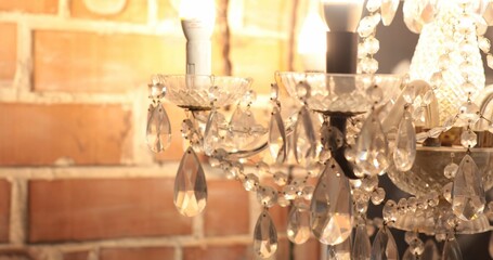 Defocused glowing elegant chandelier with diamond shaped crystal pendants look like jewelry. Victorian style glass lamp at brick wall background. Luxury interior lighting abstract background