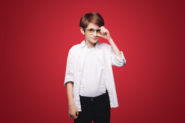 Front view of a concentrated child holding glasses and looking at camera isolated on a red background. School children