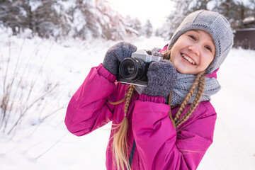 Portrait of smiling teenage girl with long pigtails in warm clothes, holding camera in hands,...