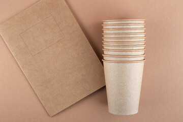 Disposable cups and notebook. Free space for your brand. Glasses, notebook and background are made of craft paper. View from above