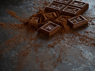 close-up pieces of chocolate with cocoa powder on dark background
