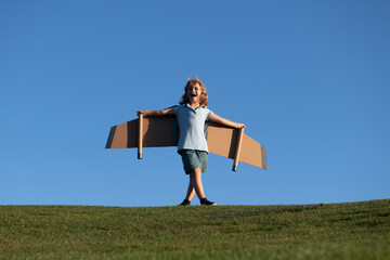Child flying in plane made craft of cardboard wings, kid boy playing outdoor. Dream, imagination, childhood. Travel and summer vacation concept.