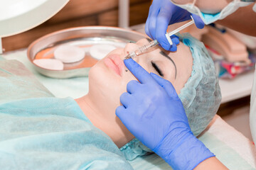 Lip augmentation. Beautician injects hyaluronic acid into the lips of a girl with a syringe. The...