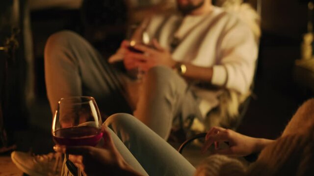 A young couple sits in armchair by fireplace . they have red wine glass in their hands. 4K. cinematic shot. slow motion.