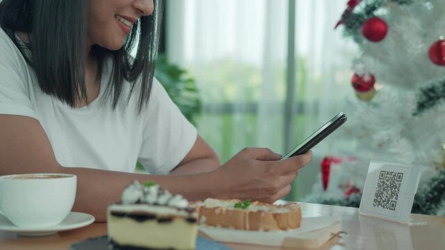 women use phones to scan a qr code to select a menu or scan to receive a discount or pay for food and drink inside a cafe. using the phone to transfer money or pay online without cash concept.