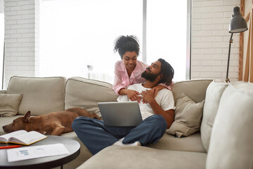 Woman hug boyfriend who work on sofa with dog