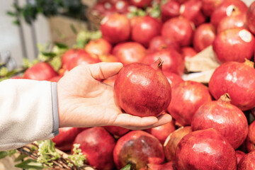 A man holding a pomegranate fruit in a supermarket close-up.