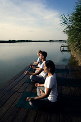 Group of people doing yoga exercises by the lake at sunset.	