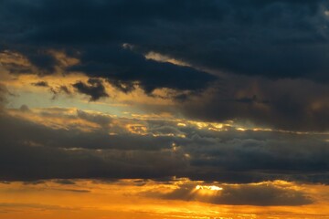 Black dramatic clouds in the sky at orange sunset, natural clouds background