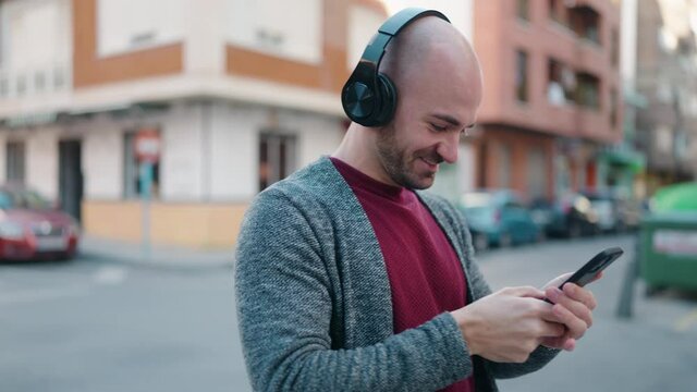 Young bald man smiling confident using smartphone and headphones at street