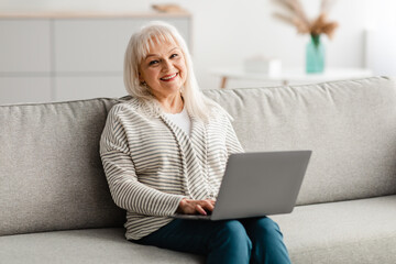 Mature woman sitting on couch and working on computer
