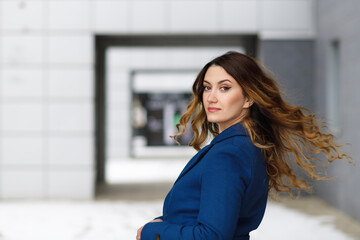 Portrait of a young charming woman in a blue coat on a city landscape background
