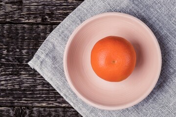 Tangerine in a white clay bowl on a gray cloth napkin on an old wooden table surface. Flat lay