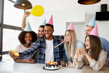 Cheerful group of diverse friends taking selfie while having birthday celebration with yummy cake at home