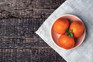 Tangerines in a white clay bowl on a gray cloth napkin on an old wooden table surface. Flat lay