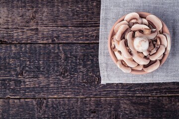 A clay bowl with sliced champignons on a gray napkin against the background of the texture of an old wood. Flat lay
