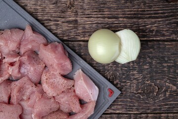Meat cut into pieces and two halves of an onion on an old textured wooden surface. Flat lay