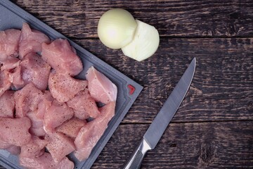 Meat cut into pieces, a knife and two halves of an onion on an old textured wooden surface. Flat lay