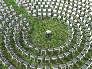 man standing in a circle of empty chairs on a green grass field