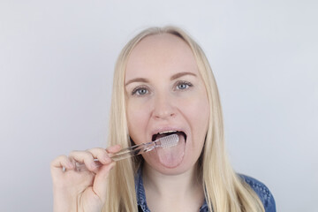 Clean tongue. Close-up of a woman performing antimicrobial hygiene with a special tongue brush. Isolated on white background. A blond female looks into the frame, as if he is looking in a mirror.