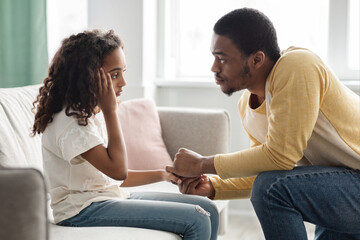 Black father comforting his upset kid, home interior
