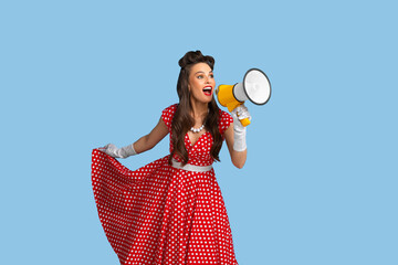 Mega sale. Agitated young pinup woman in retro clothes shouting into megaphone on blue studio background