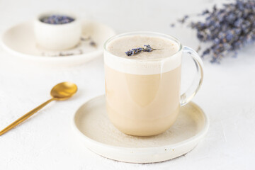 Lavender latte coffee with coconut milk in a glass mug on a light table.