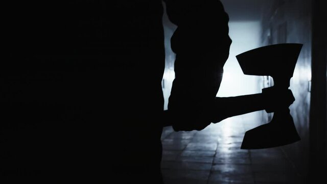 The gloomy figure of the executioner moves along the dark corridor towards the light. Only a figure is visible, he is holding a large double-sided ax, the man plunges into the light.