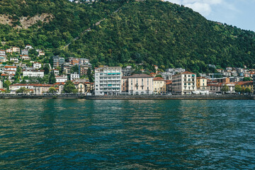 Fototapeta na wymiar Panoramic view of big houses over hill town by the lake shore in northern Italy and boat passing 