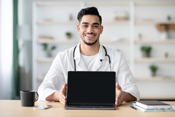 Middle-eastern man doctor showing laptop with blank screen, mockup
