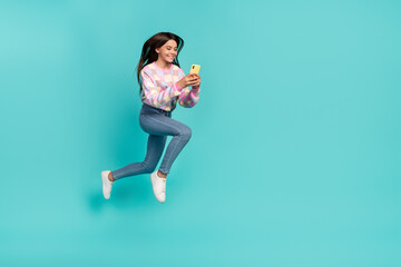 Full length body size view of pretty trendy cheery girl jumping using device chatting isolated on vivid teal turquoise color background
