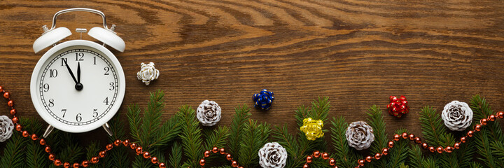 White alarm clock, cones, fir twigs and beads garland on brown wooden table background. Empty place for text. Countdown to midnight. Counting last moments before Christmas or New Year. Top down view.