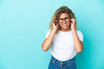 Girl with curly hair isolated on blue background frustrated and covering ears