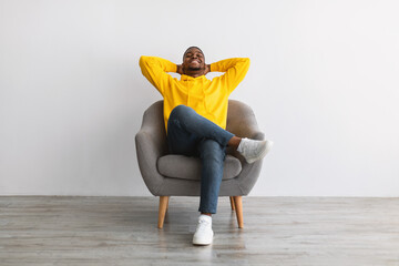 African American Guy Relaxing Sitting In Comfortable Armchair, Gray Background