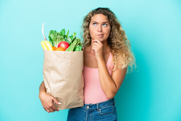 Girl with curly hair holding a grocery shopping bag isolated on green background having doubts and thinking