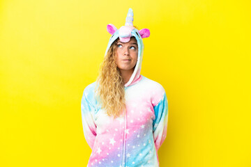 Girl with curly hair wearing a unicorn pajama isolated on yellow background and looking up