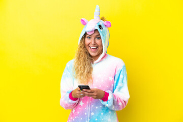Girl with curly hair wearing a unicorn pajama isolated on yellow background surprised and sending a...
